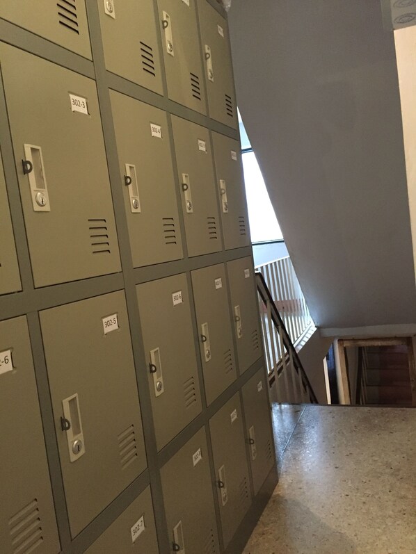 A row of metal lockers with numbered labels, a staircase, and a railing. - Room Bangkok - Hostel (Bangkok)