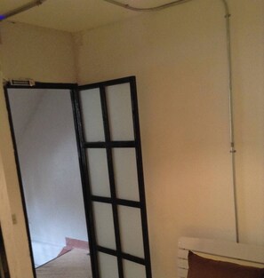 A room with a bed, a white wall, and a door with a black frame. - Room Bangkok - Hostel (Bangkok)