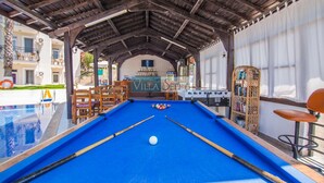 A pool table with a billiards cue, a foosball table, and a bar area with a sign reading "VILLA SEPELTINA".