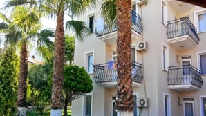 A multi-story building with balconies, surrounded by palm trees and greenery.