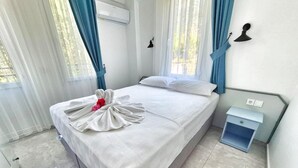 A hotel room with a large bed, a bedside table, a wall-mounted air conditioner, and a window with blue curtains.