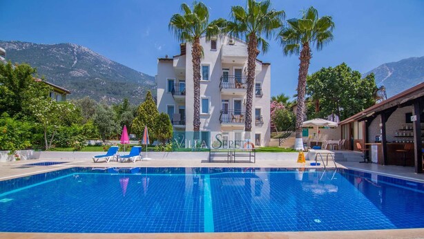 A hotel with a swimming pool, palm trees, and a mountain backdrop.
