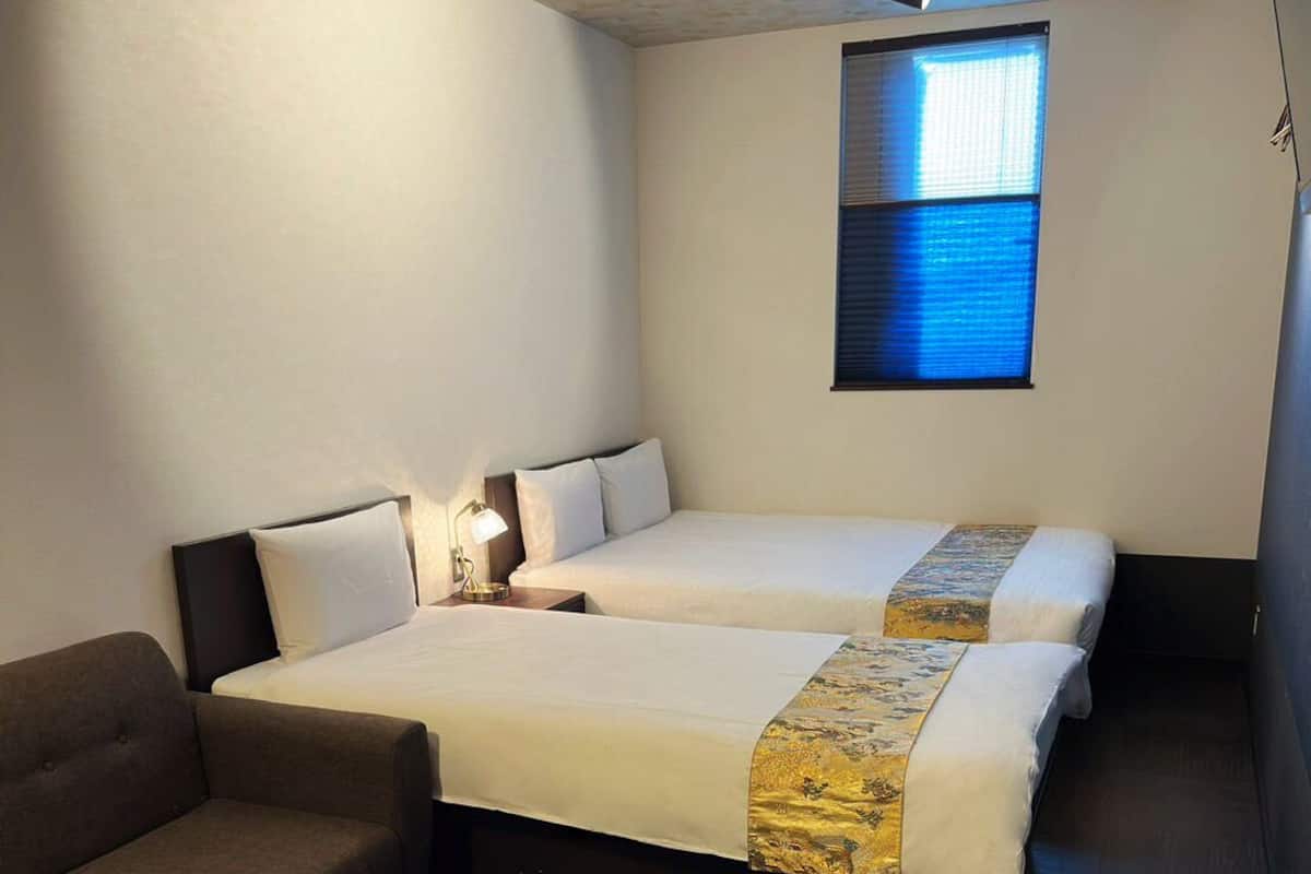 A hotel room with two beds, a sofa, a small round table, and a window with blinds.