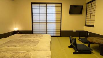 A traditional Japanese room with tatami flooring, a futon bed, sliding shoji doors, and a television mounted on the wall.