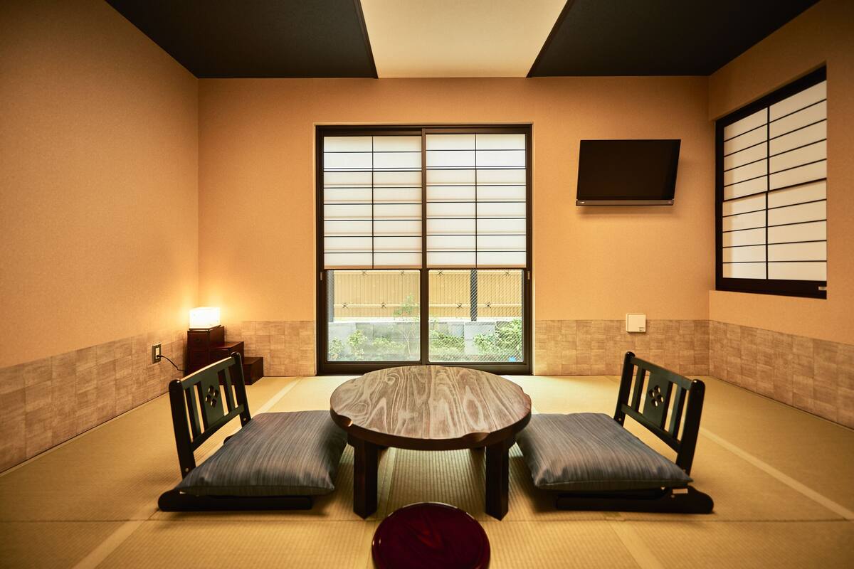 A tatami room with a low table and benches, large windows, and a wall-mounted TV.