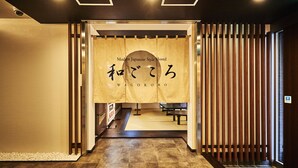 Entrada de un hostal de estilo japonés moderno con esteras de tatami, un panel biombó de papel y una partición de listones de madera.