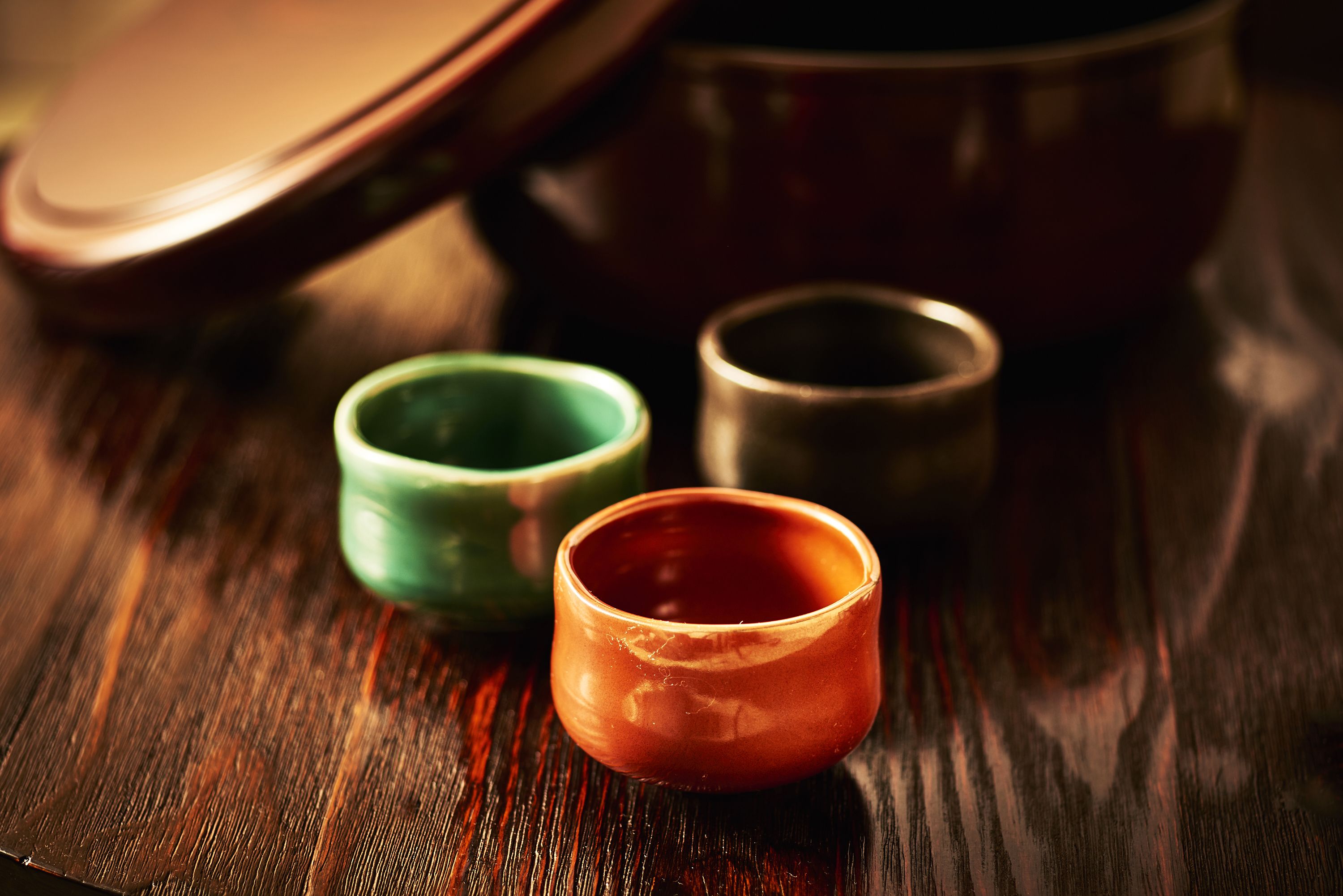 Una mesa de madera con tres tazas de cerámica de distintos colores.