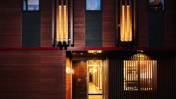 Fachada de ladrillo rojo, puerta de madera y un camino empedrado que conduce a un interior bien iluminado.