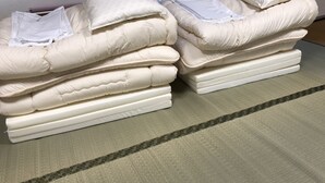 Una pila ordenada de colchones y almohadones blancos sobre un piso con textura, probablemente en una habitación de hotel.