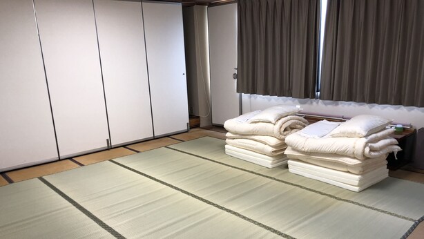 Una habitación con esteras de tatami, un armario y ropa de cama apilada ordenadamente.