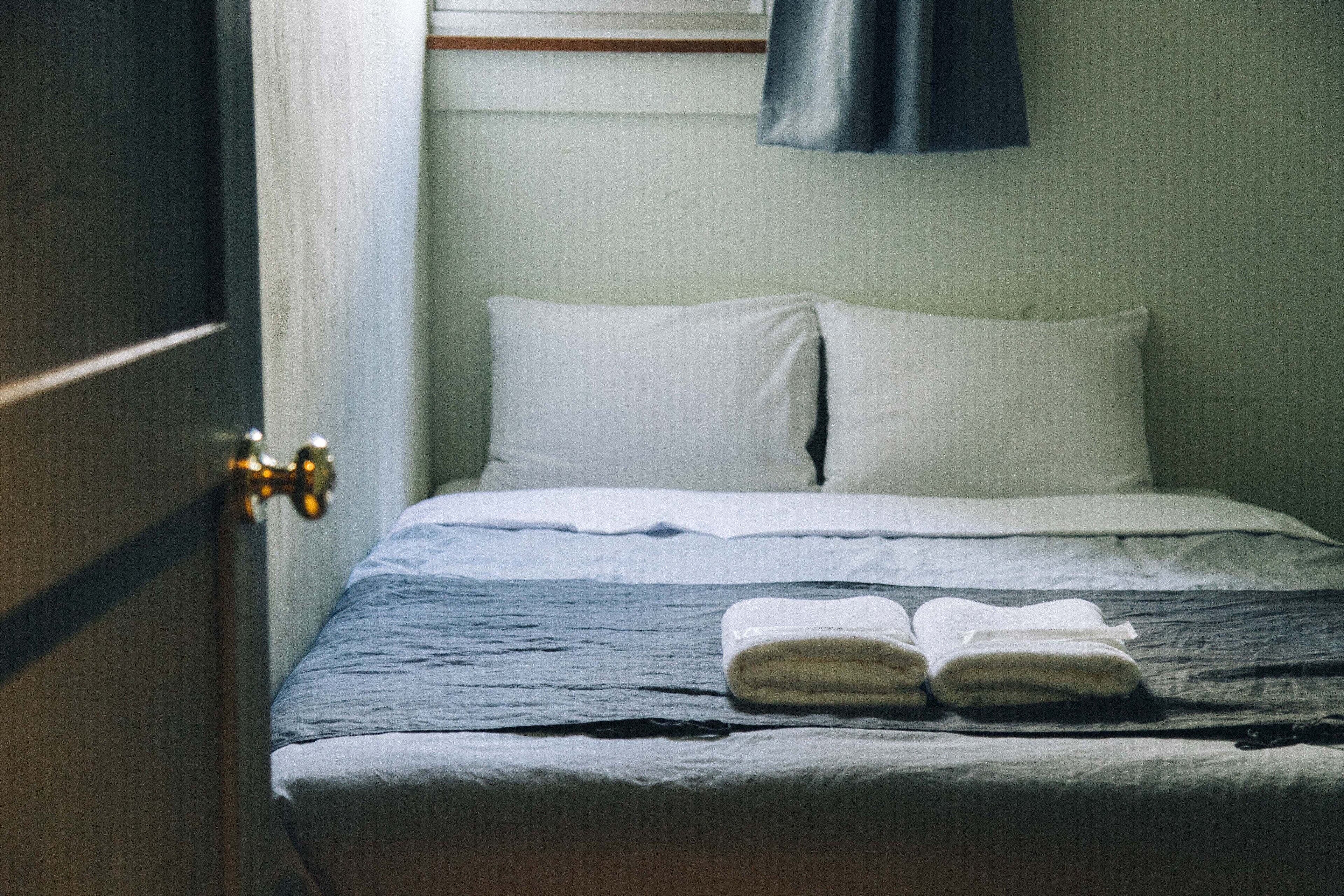 A bed with white linens and a folded towel on it.