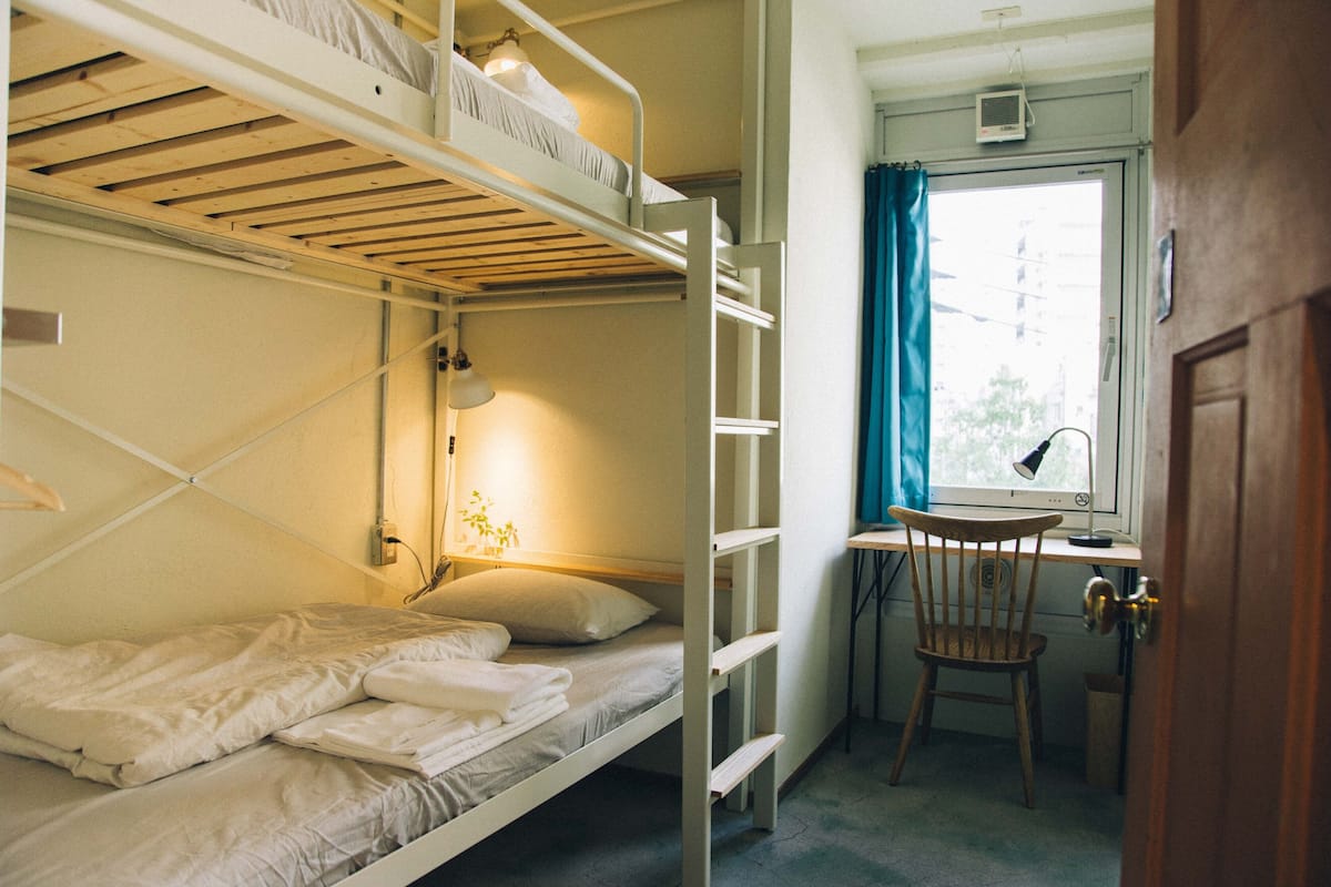 Habitación con literas, un escritorio, una silla, una ventana con cortinas y una puerta.