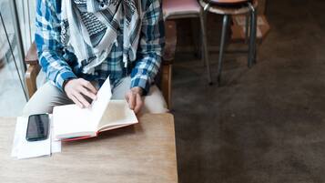 A person sitting at a wooden table with a book and a smartphone.