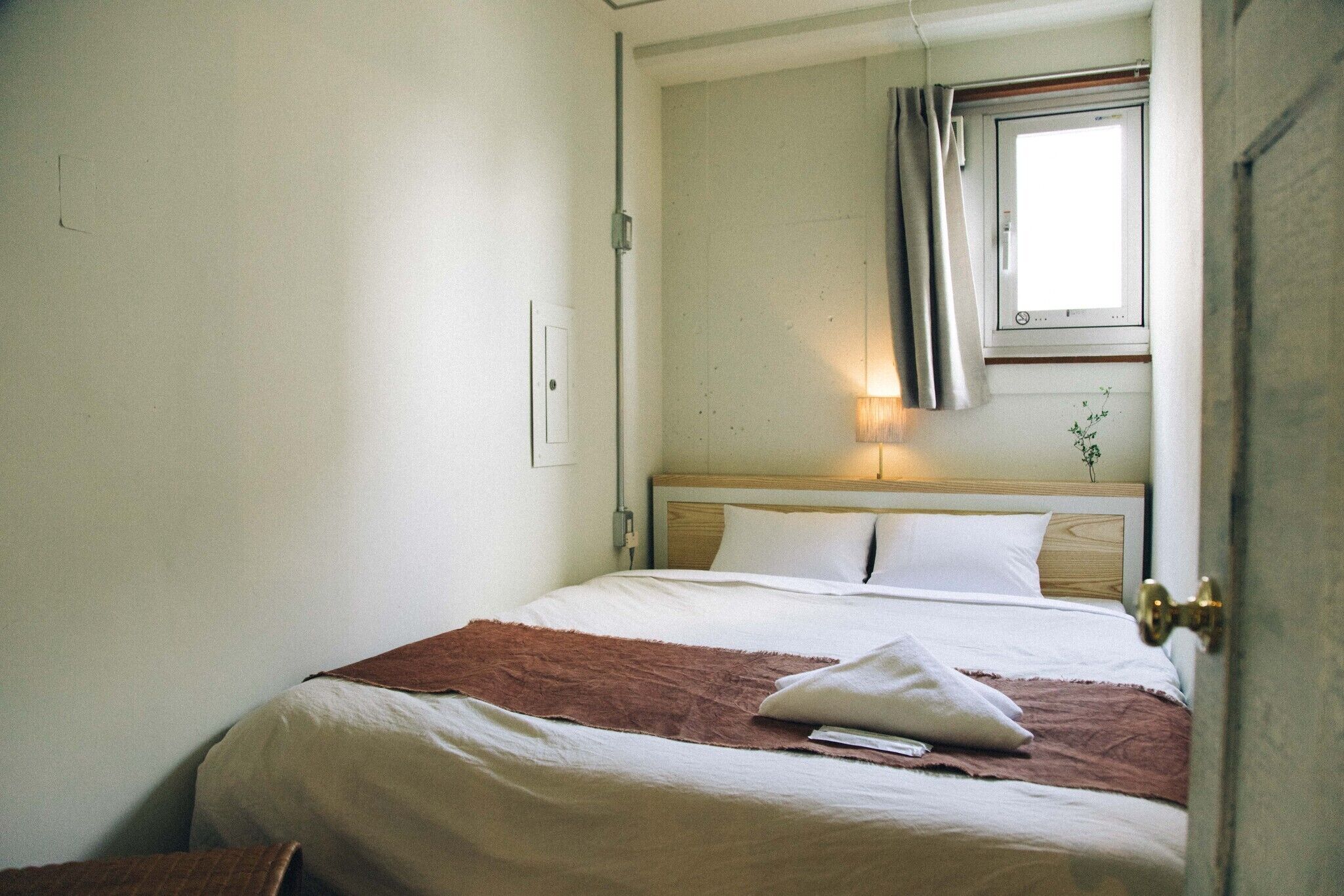 Un dormitorio con cama, ventana con cortinas, lámpara de noche y una puerta.