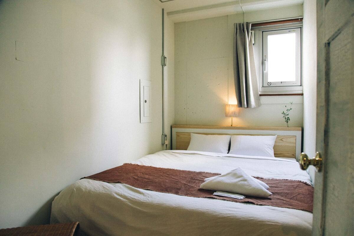 Un dormitorio con cama, ventana con cortinas, lámpara de noche y una puerta.