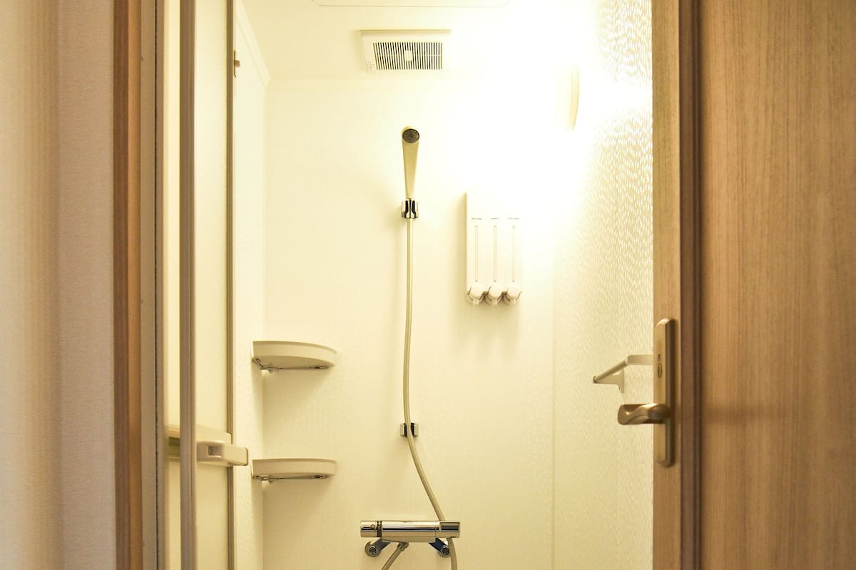 Ein kleiner, abgeschlossener Duschbereich mit Handbrause, Handtuchhalter und Lüftungsventil.