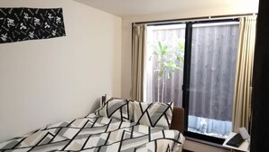 Une chambre à coucher avec un lit, un bureau avec un ordinateur portable et une fenêtre avec des rideaux.
