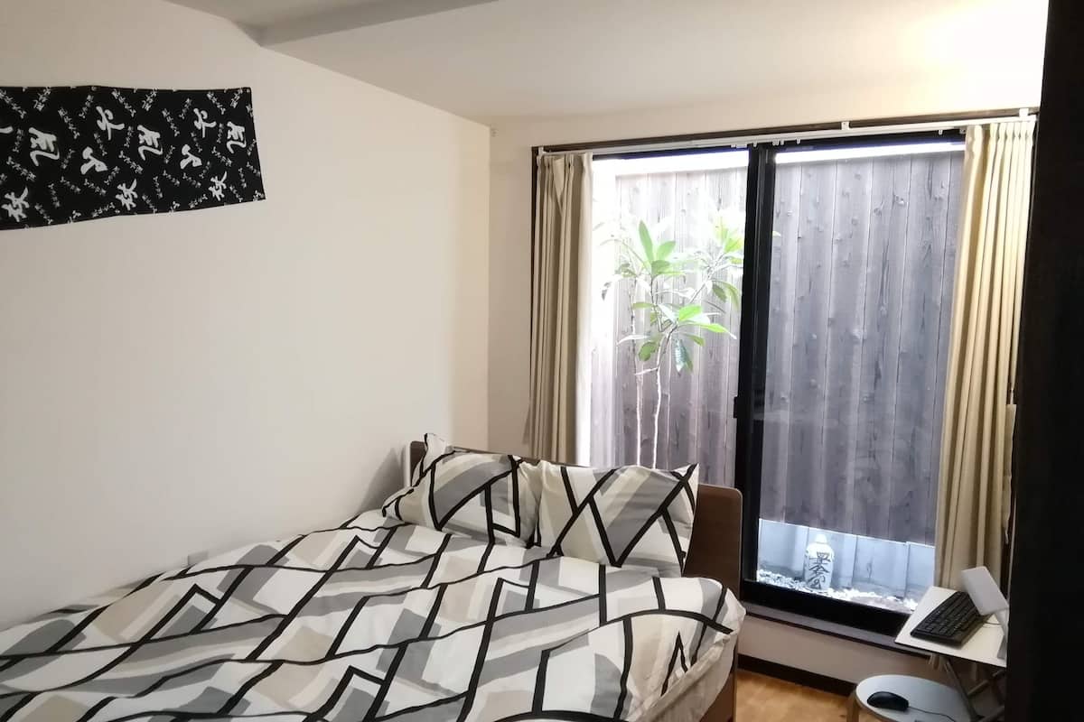Een slaapkamer met een bed, een bureau met een laptop en een raam met gordijnen.