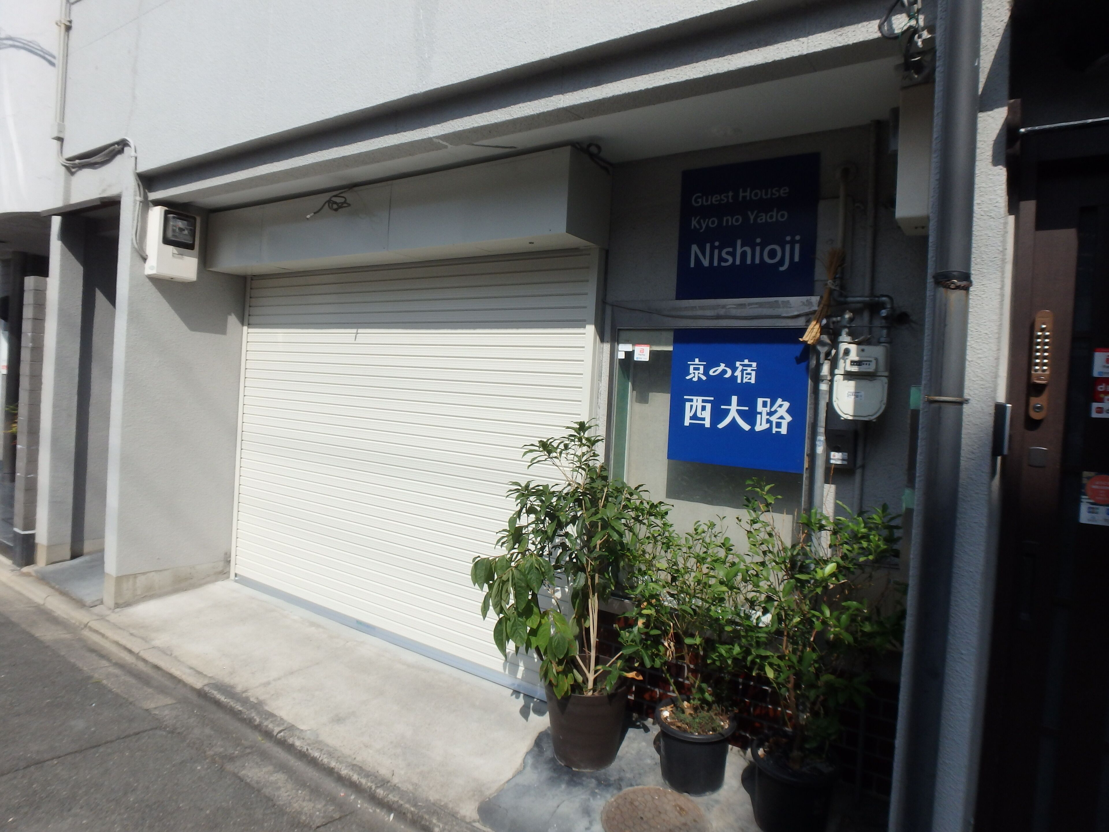 Een gesloten winkelgevel met een blauw bord waarop staat 'Guest House Nishioji'.