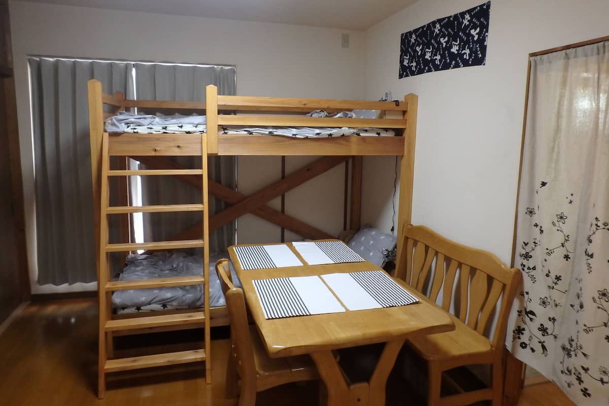 Een stapelbed met een tafel en stoelen in een kamer met gordijnen en een wanddecoratie.