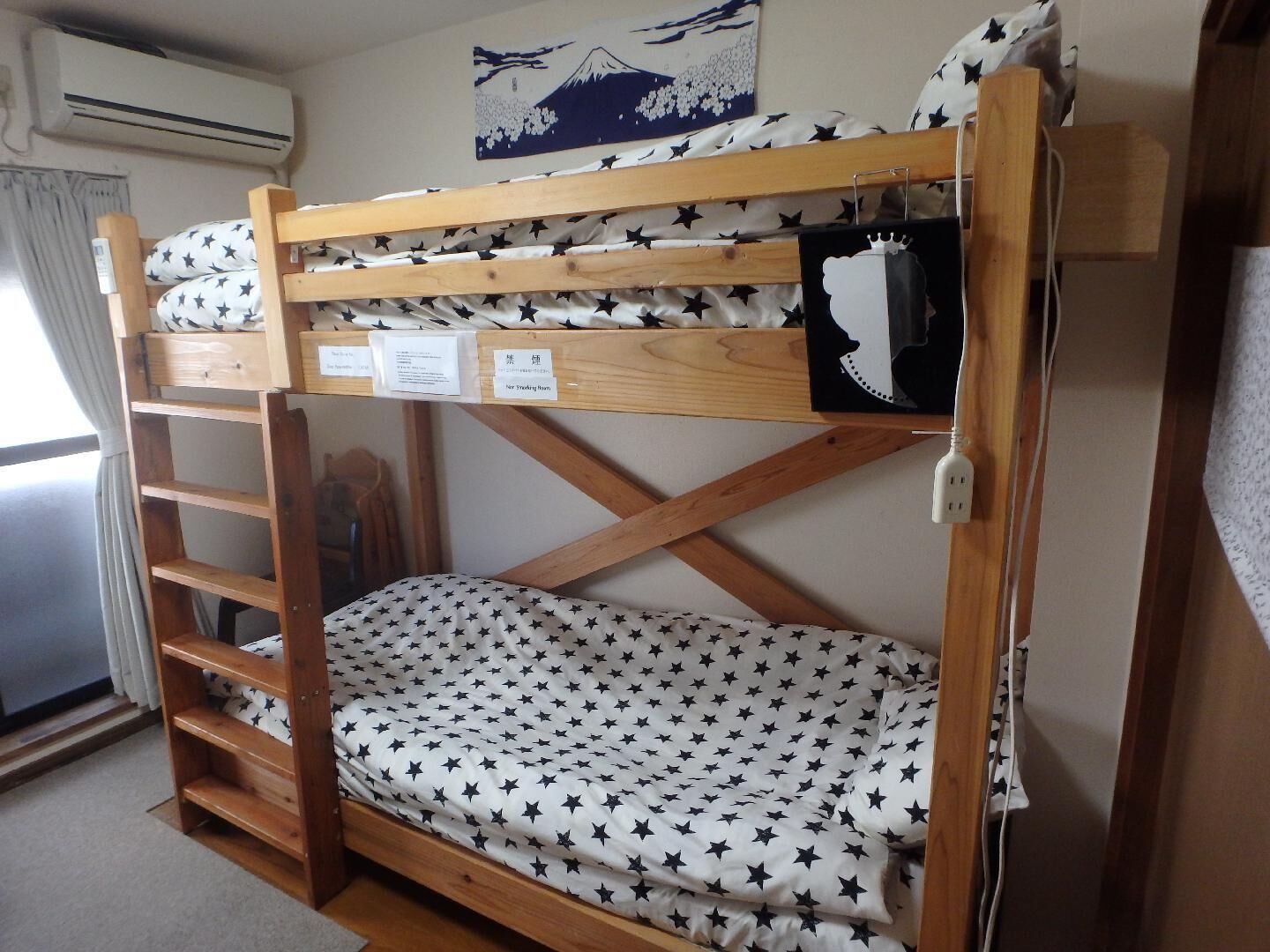 Un lit superposé avec un matelas orné de motifs en forme d’étoiles, une échelle en bois et un climatiseur fixé au mur.