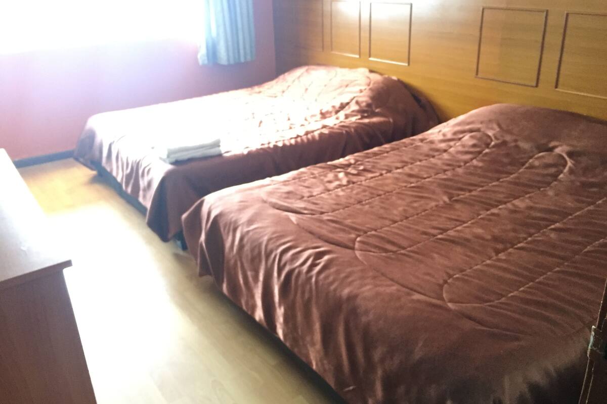 Une chambre d’hôtel avec deux lits, une tête de lit en bois et une commode en bois.