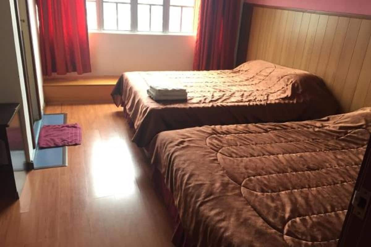 Une chambre avec deux lits, un plancher en bois, une fenêtre avec des rideaux rouges et une porte.