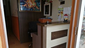 Een receptiebalie met een houten afwerking en een witte paneel, een zwarte bureaustoel, een ingelijst kunstwerk aan de muur, en een agenda aan de muur.