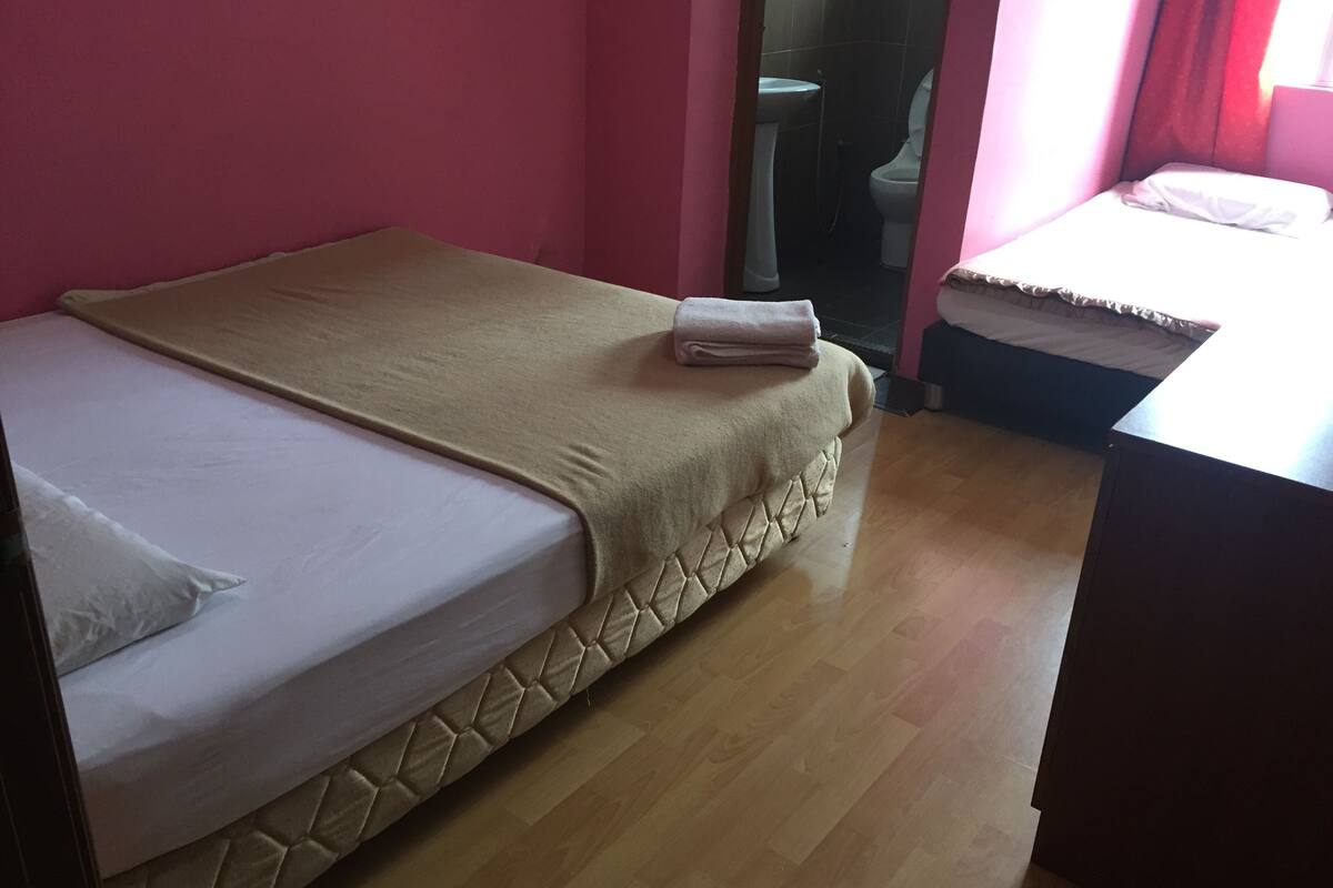 Une petite chambre avec un lit simple, un plancher en bois, une couvre-lit beige et un oreiller blanc.