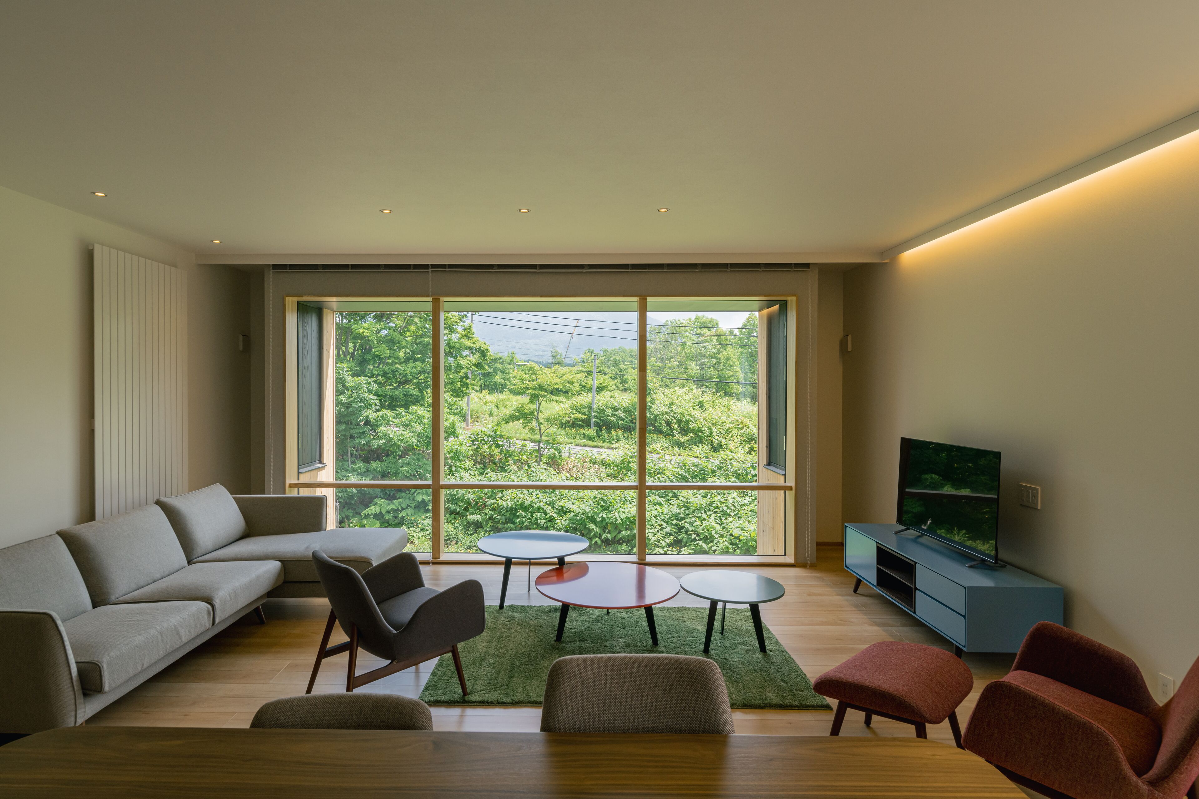 A modern living room with a large window, a sofa, a coffee table, a TV stand, and a dining table.