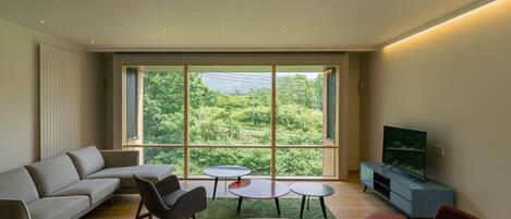 A modern living room with a large window, a sofa, a coffee table, a TV stand, and a dining table.