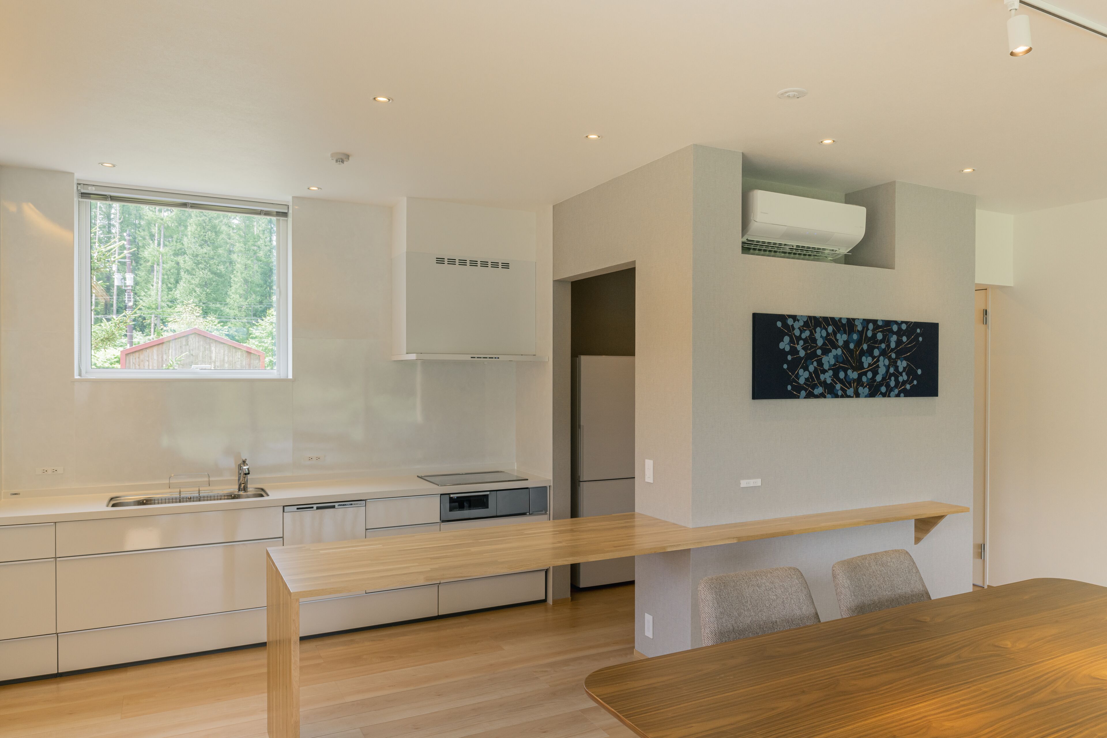A modern kitchen with white cabinetry, a wooden dining table, and recessed lighting.