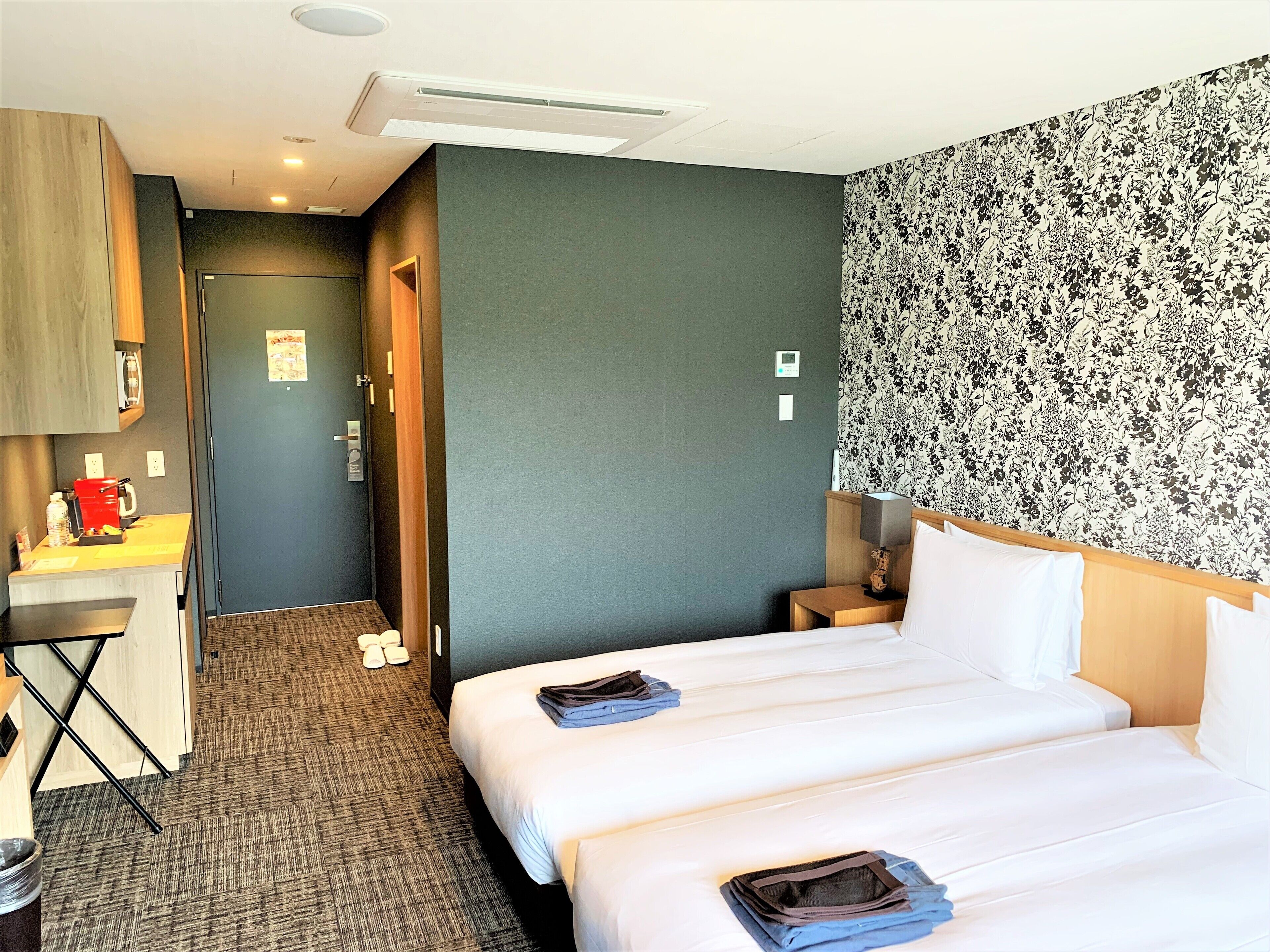 A hotel room with two beds, a desk, a chair, a wardrobe, and a bathroom.