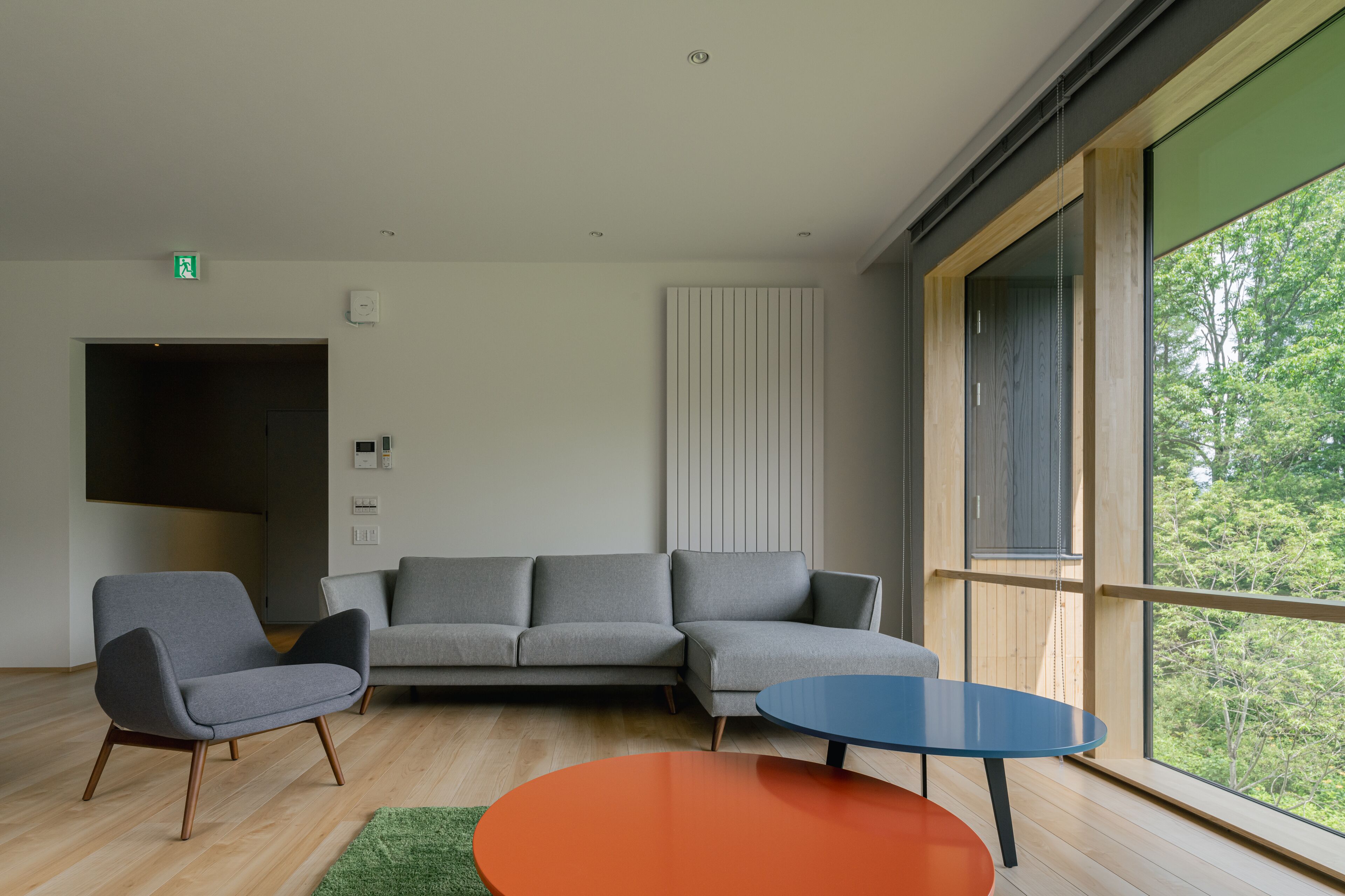 A modern living room with a sectional sofa, a round orange table, and a large window with a view of trees.