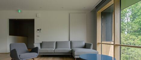 A modern living room with a sectional sofa, a round orange table, and a large window with a view of trees.