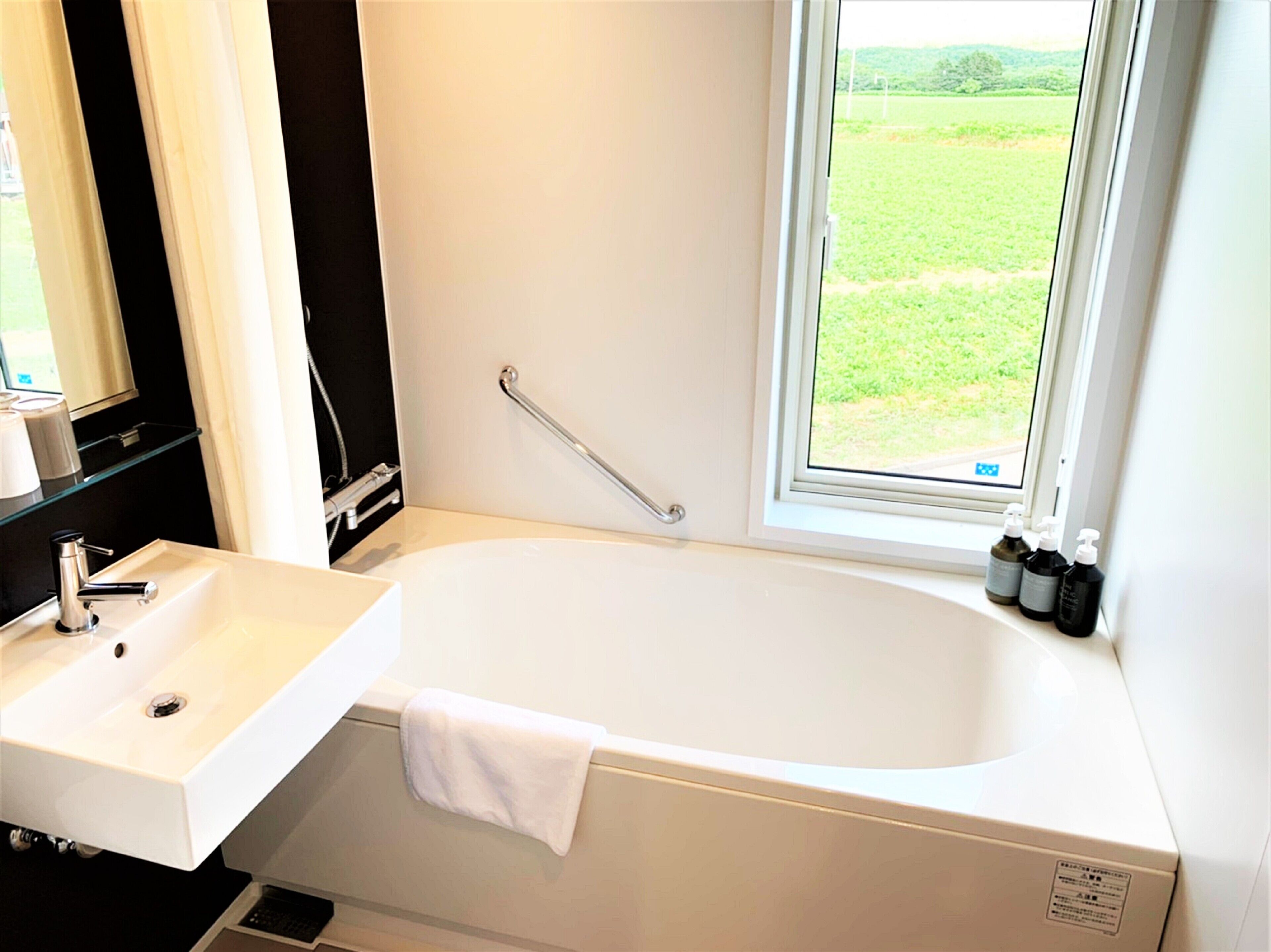 Une salle de bain avec une baignoire blanche, un lavabo et une fenêtre donnant sur un champ verdoyant.
