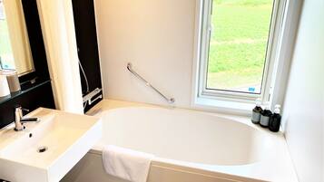 Une salle de bain avec une baignoire blanche, un lavabo et une fenêtre donnant sur un champ verdoyant.