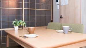 Uma mesa de madeira com um vaso de planta, duas canecas e um prato numa divisão com parede em azulejo e uma porta com um aviso.
