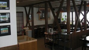 A restaurant interior with exposed wooden beams, framed pictures on the walls, and a bar area with stools. - Lodge Christmas Rose ZAO (Yamagata)
