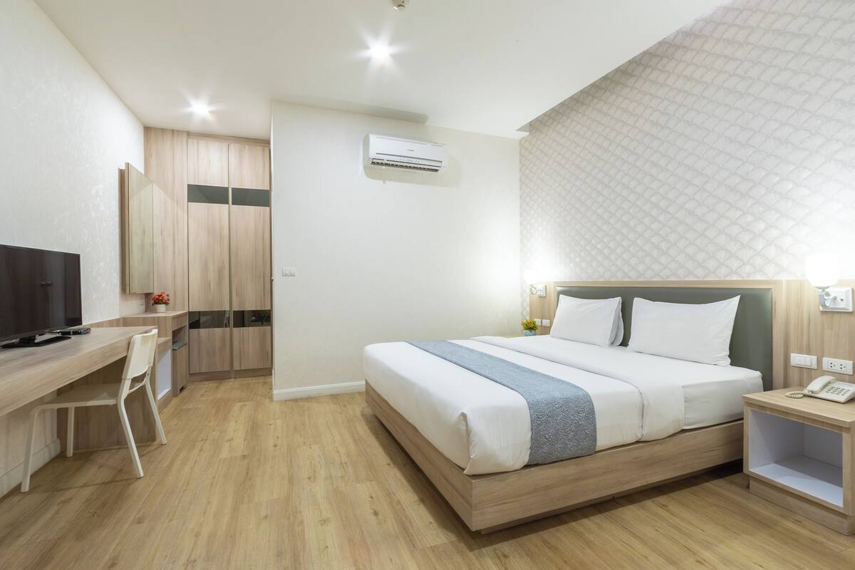 Une chambre d’hôtel moderne avec un lit en bois, un bureau avec une chaise, une télévision et une petite table de chevet avec un téléphone.