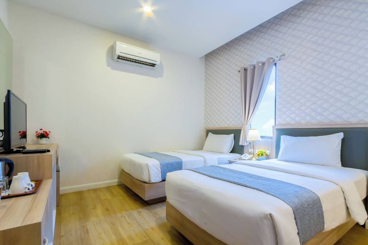 Une chambre d’hôtel avec deux lits, un bureau équipé d’un ordinateur et d’une machine à café, un climatiseur et une fenêtre avec des rideaux.