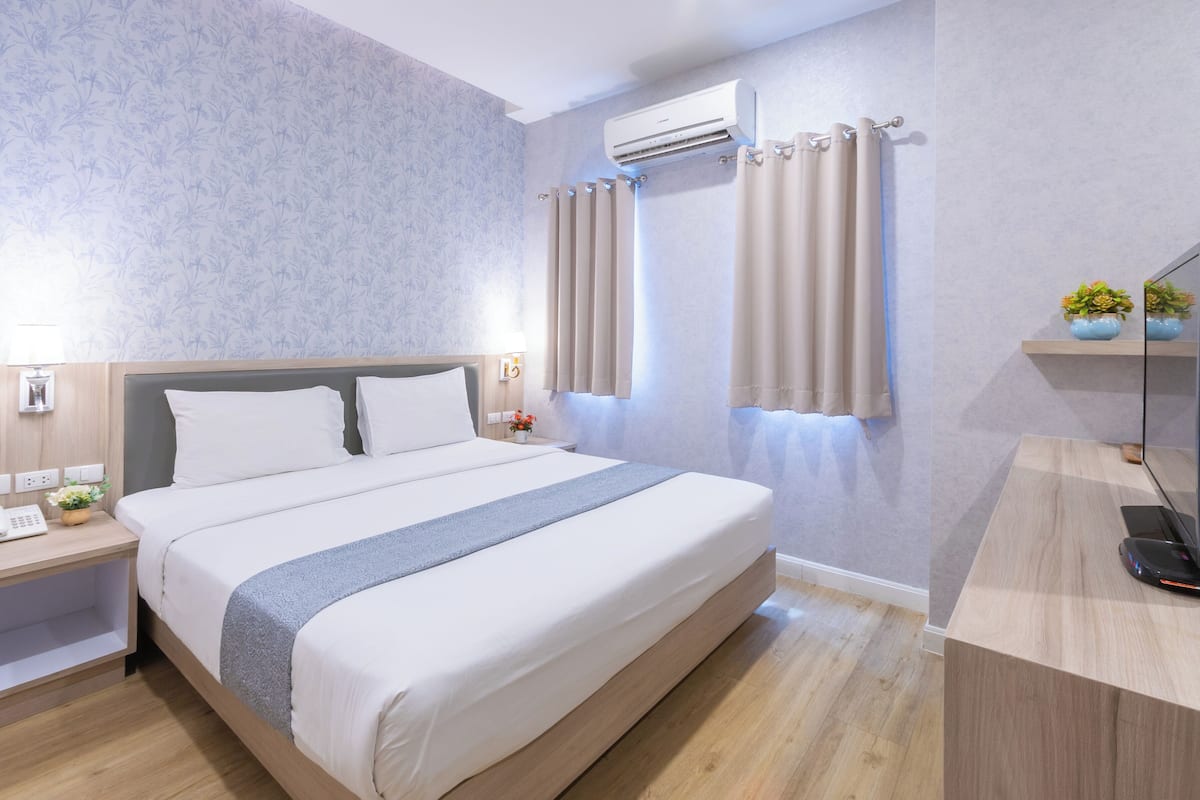 Un lit bien fait, recouvert d’une couverture grise, une table de chevet avec une lampe et un climatiseur fixé au mur.