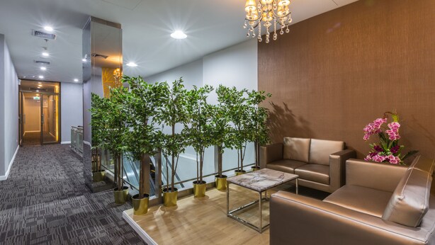 Un lobby moderno con mostrador de recepción, zona de estar, plantas en macetas y un candelabro.