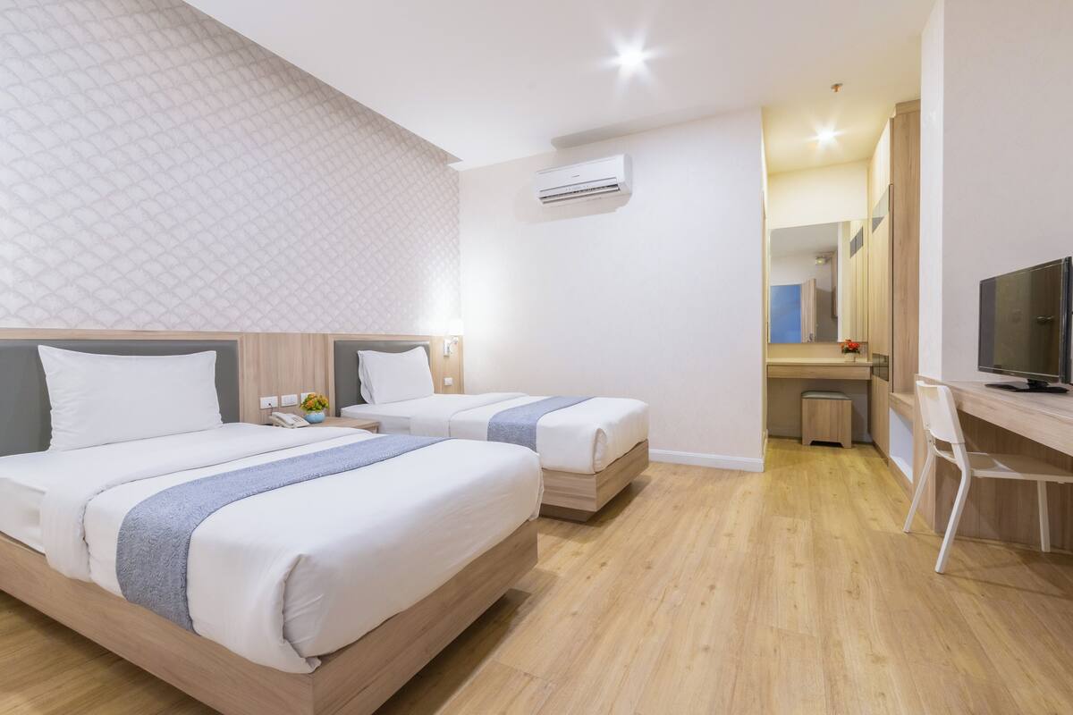 Une chambre d’hôtel avec deux lits, un bureau, une chaise, un appareil de climatisation et un téléviseur.