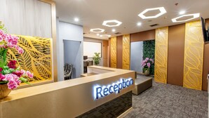 Un área de recepción con un mostrador de madera, un letrero que dice 'Reception' y paneles decorativos con diseños de hojas.
