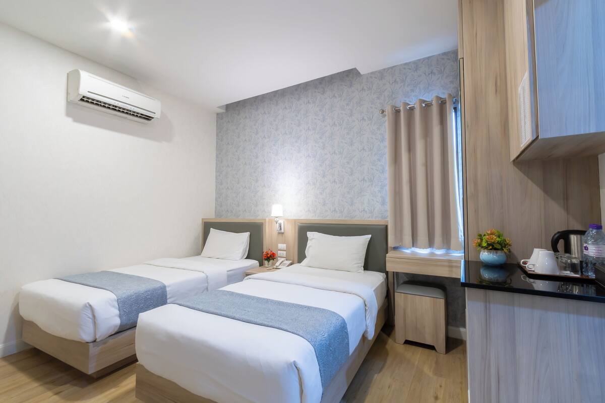 Une chambre d’hôtel avec deux lits, une petite kitchenette, une salle de bain avec rideau de douche et un appareil de climatisation.