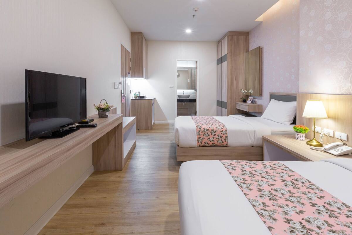 Une chambre d’hôtel équipée d’une télévision, d’un bureau, d’une table de chevet avec une lampe et de deux lits recouverts de couvre-lits à motifs floraux.
