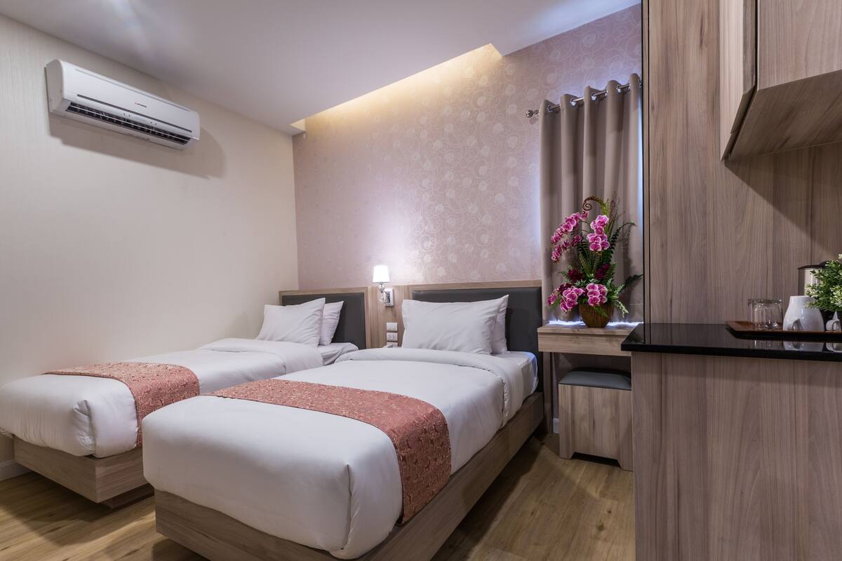 Une chambre d’hôtel avec deux lits, un bureau, une lampe, un vase et un appareil de climatisation.