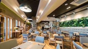 A modern restaurant with wooden flooring, blue chairs, and a green wall with plants. - Nadee 10 Resort & Hotel (Khon Kaen)