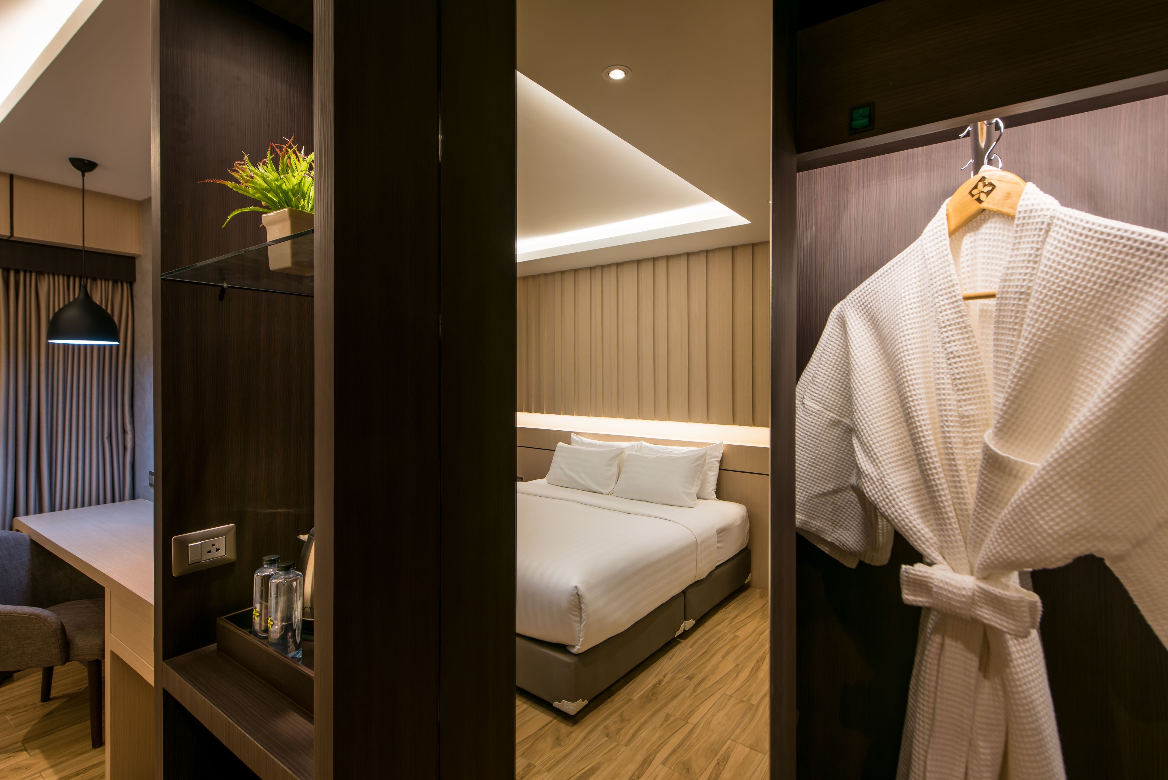 Una habitación de hotel moderna con cama, mesita de noche, lámpara y una bata colgada de un perchero.